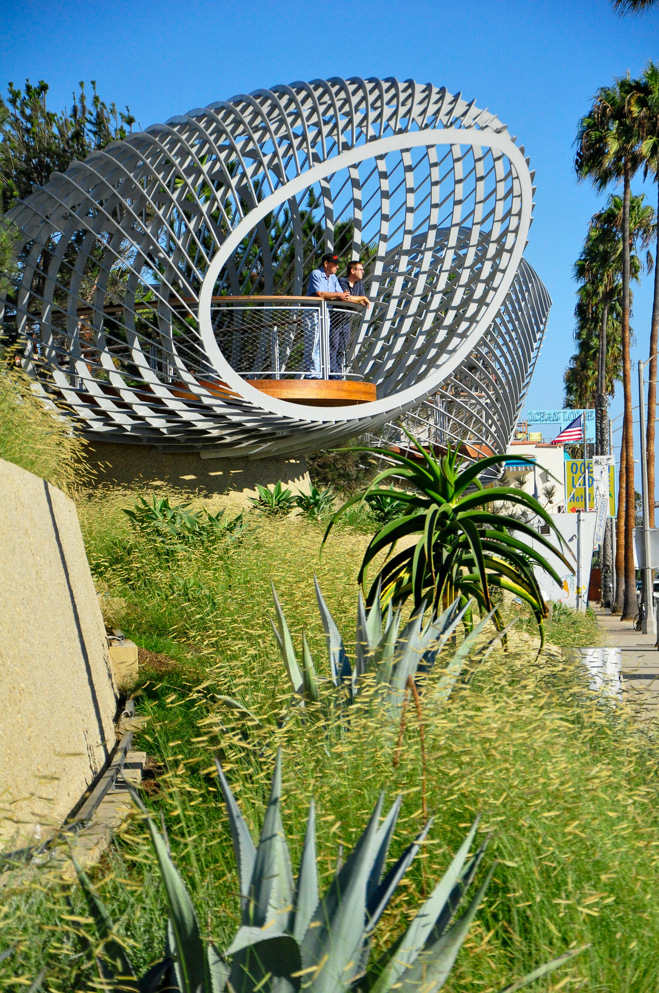 A geometric structure looking out over a swath of grass and succulents.